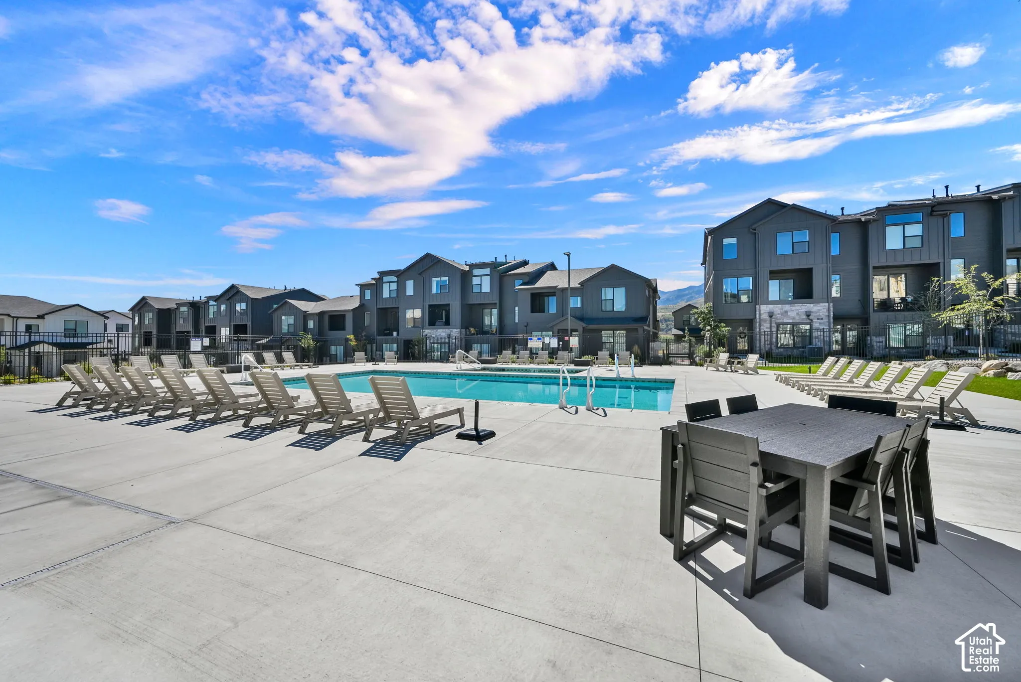 Community swimming pool with an expansive concrete deck, multiple lounge chairs, and modern multi-story buildings