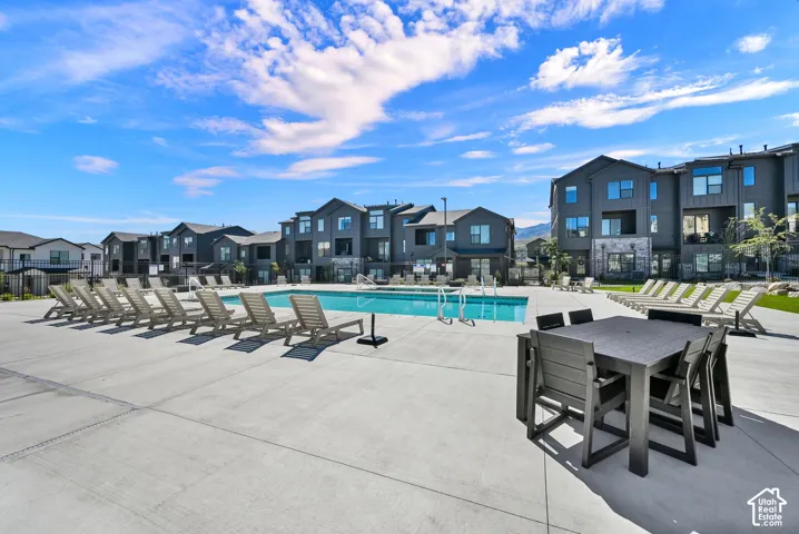 Community swimming pool with an expansive concrete deck, multiple lounge chairs, and modern multi-story buildings