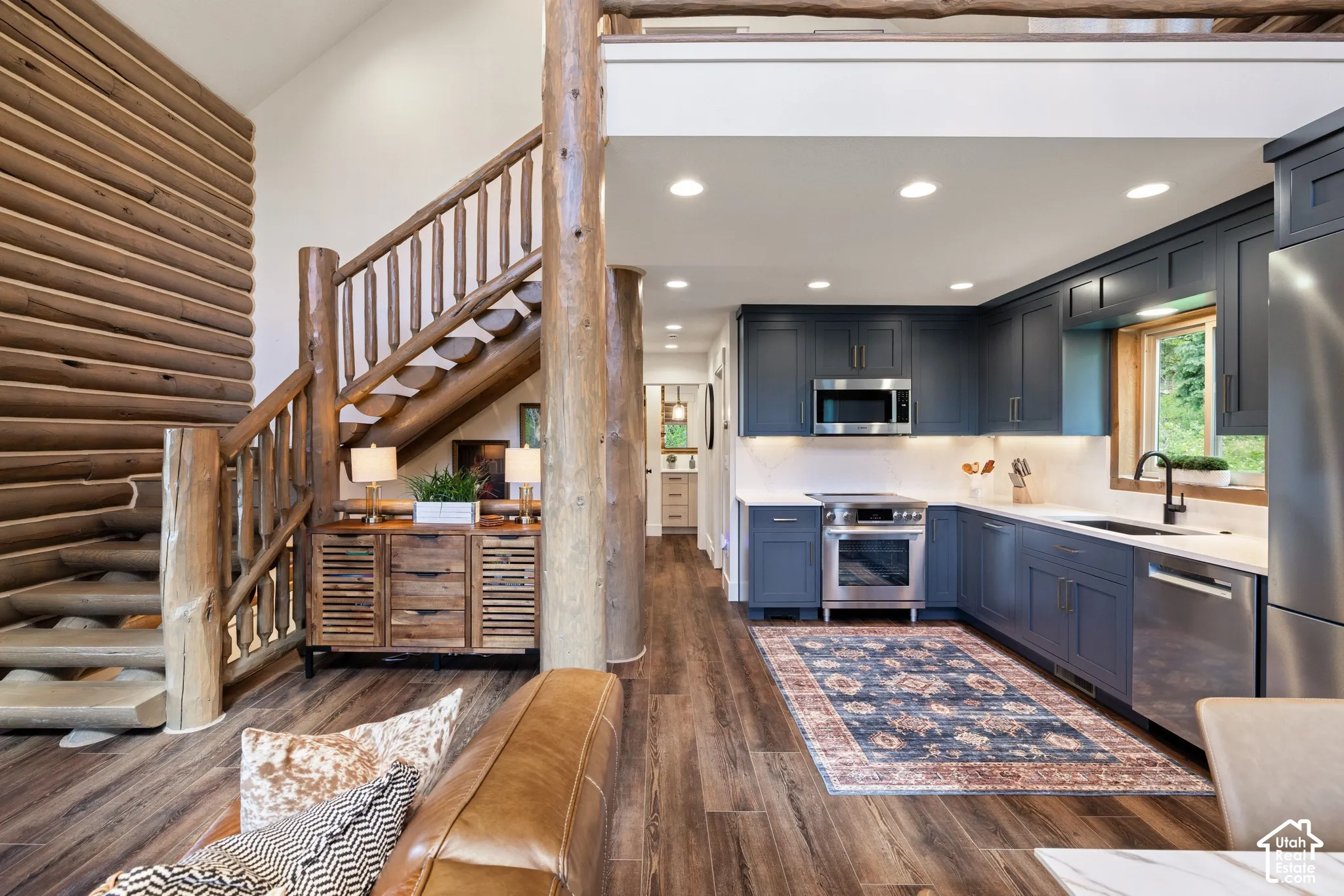 Custom log construction, wood-finish flooring, a full kitchen with dark blue cabinetry, stainless steel appliances, and white countertops