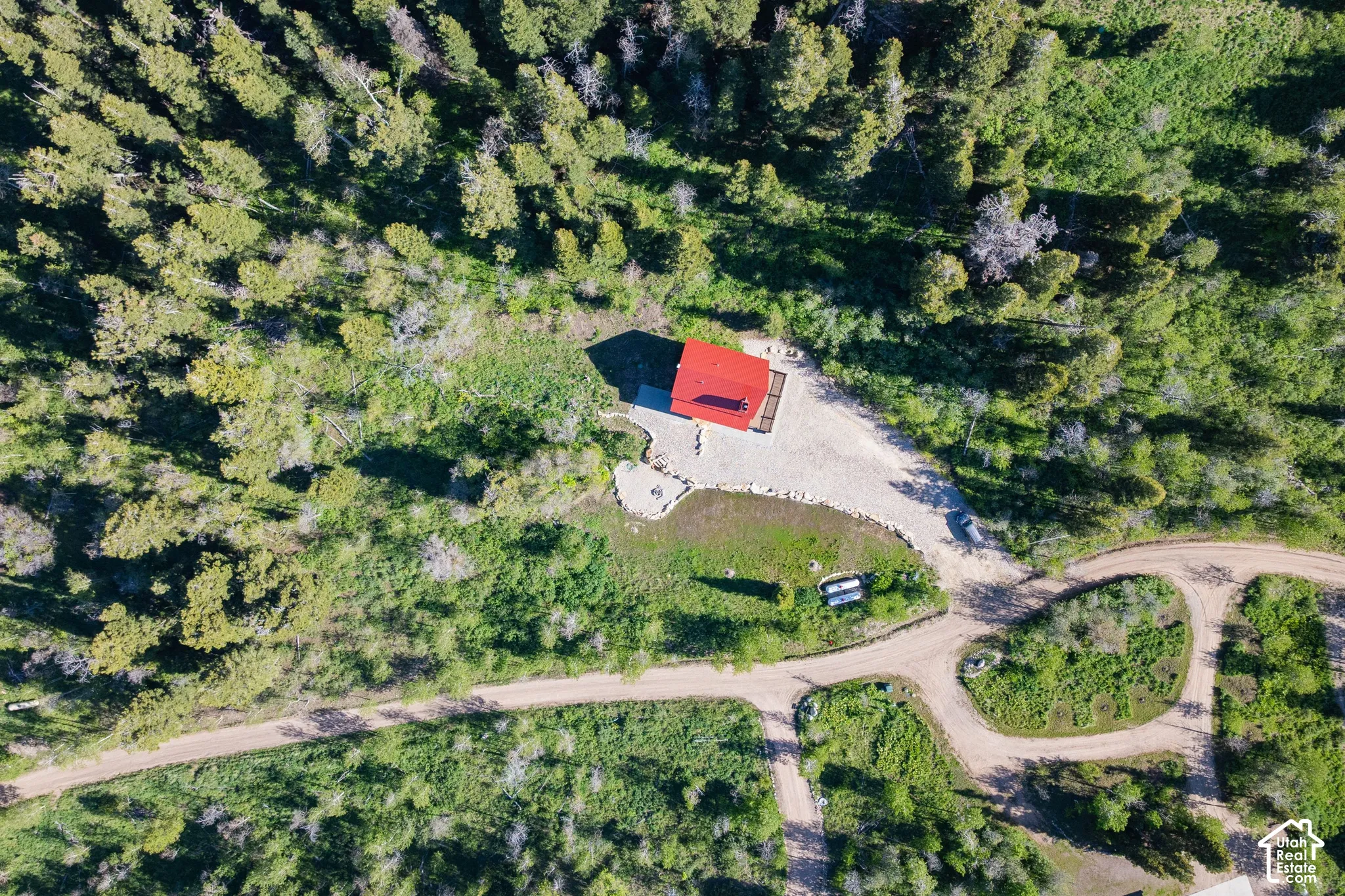 Wooded lot featuring a red-roofed structure, gravel drive, and natural landscaping