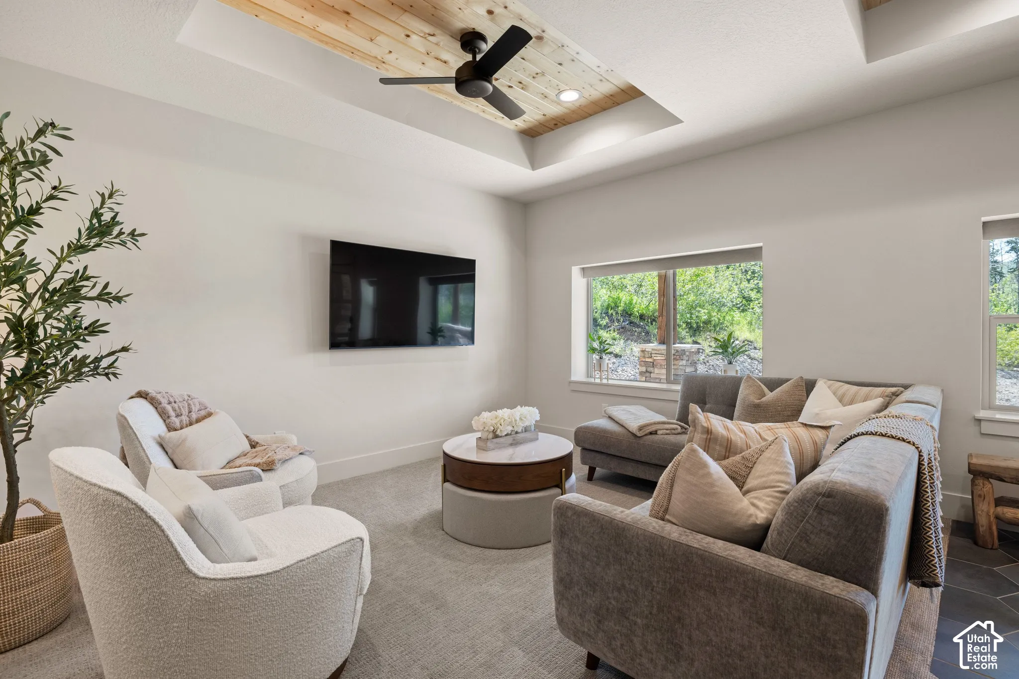 Recessed ceiling with wood-finish paneling, ceiling fan with black blades, and large windows