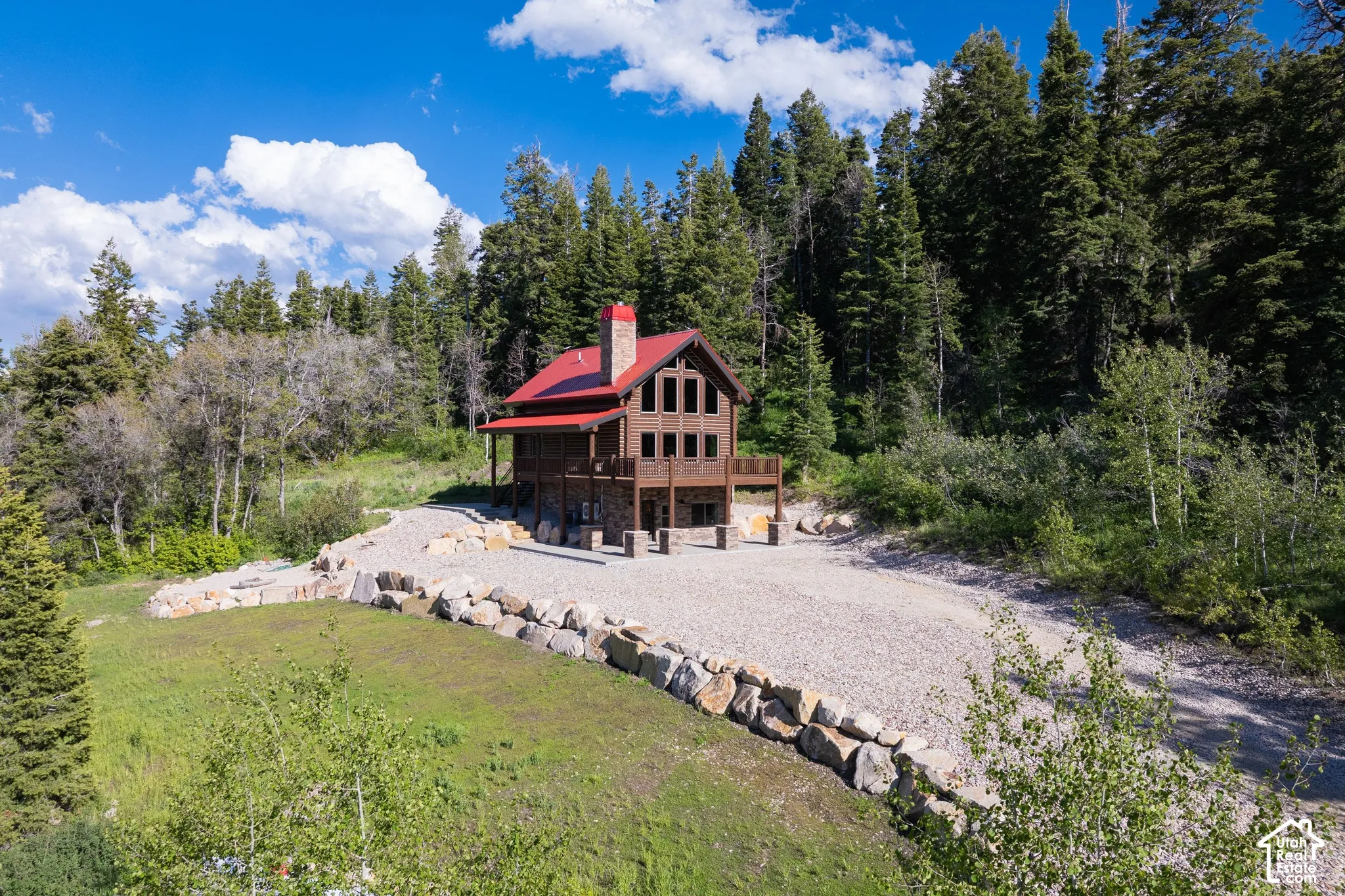 Rustic home featuring a red roof, a stone-clad chimney, and a multi-level wood deck