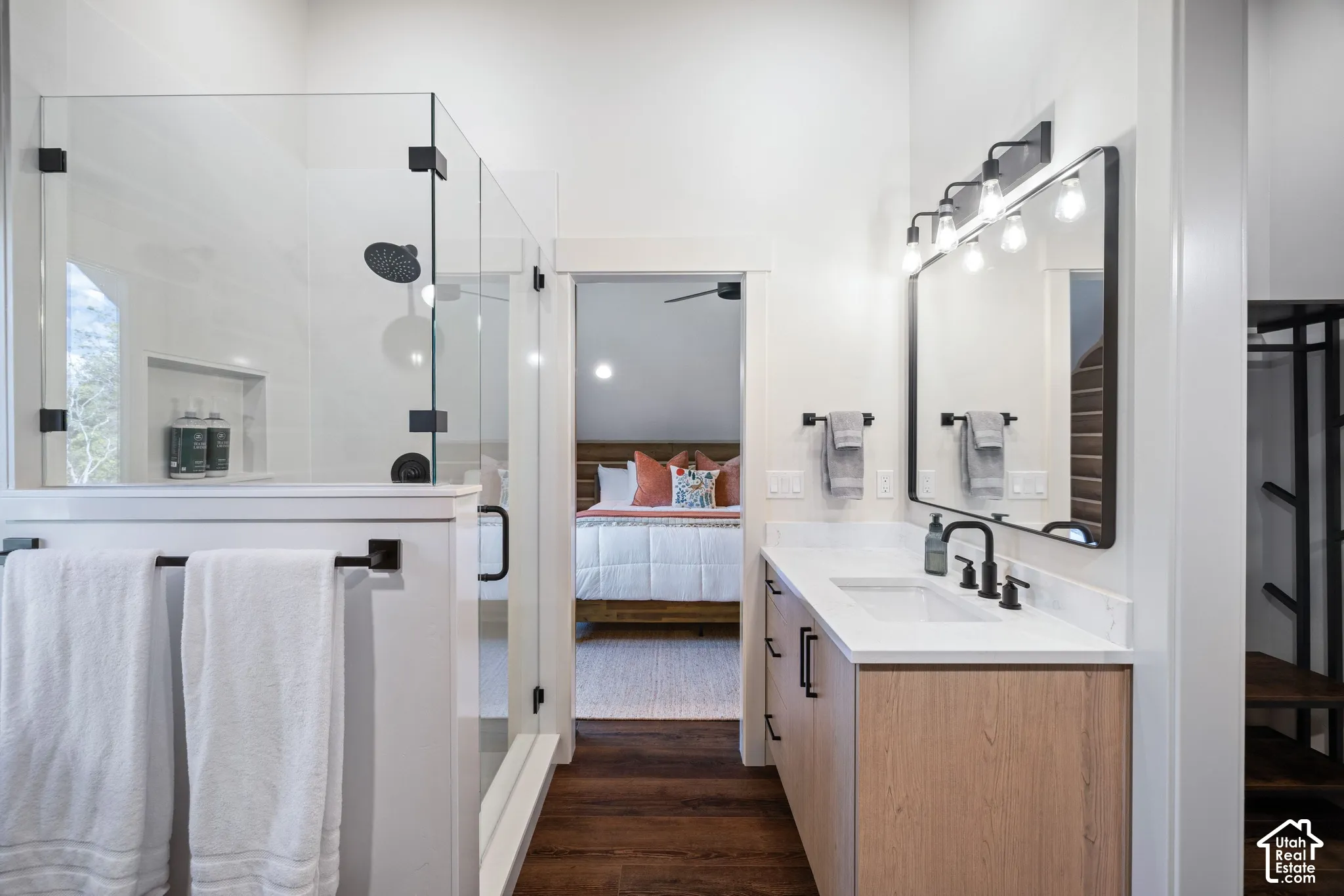 Glass-enclosed shower with matte black fixtures, single vanity with wood-finish cabinetry, white countertop, and dark wood-finish flooring