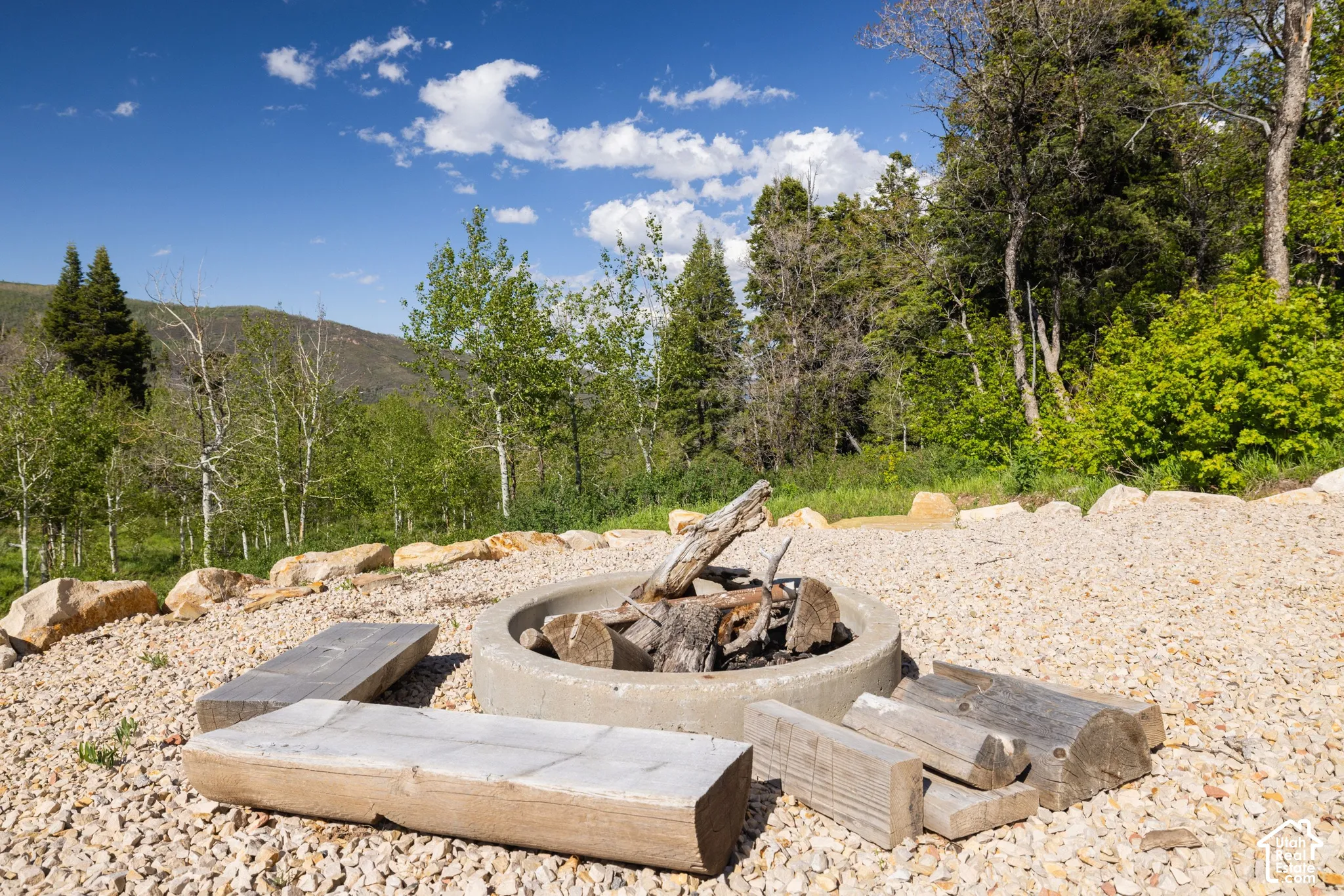 Gravel hardscaping featuring a concrete fire pit with surrounding log seating