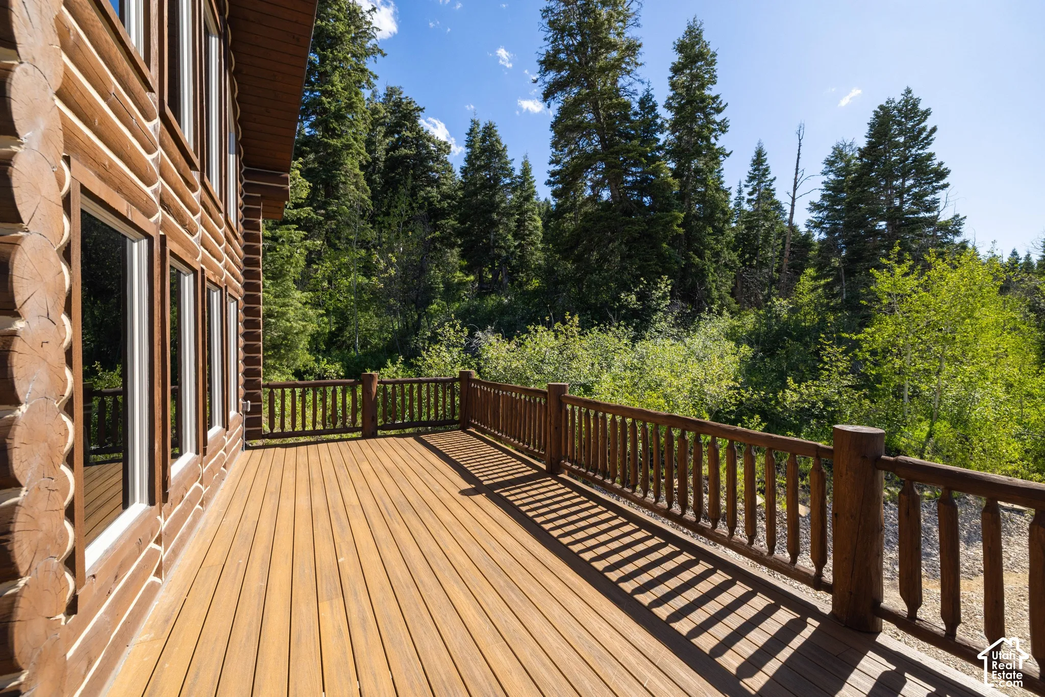 Expansive wood deck with turned wood balusters, bordered by a log-style exterior with multiple windows