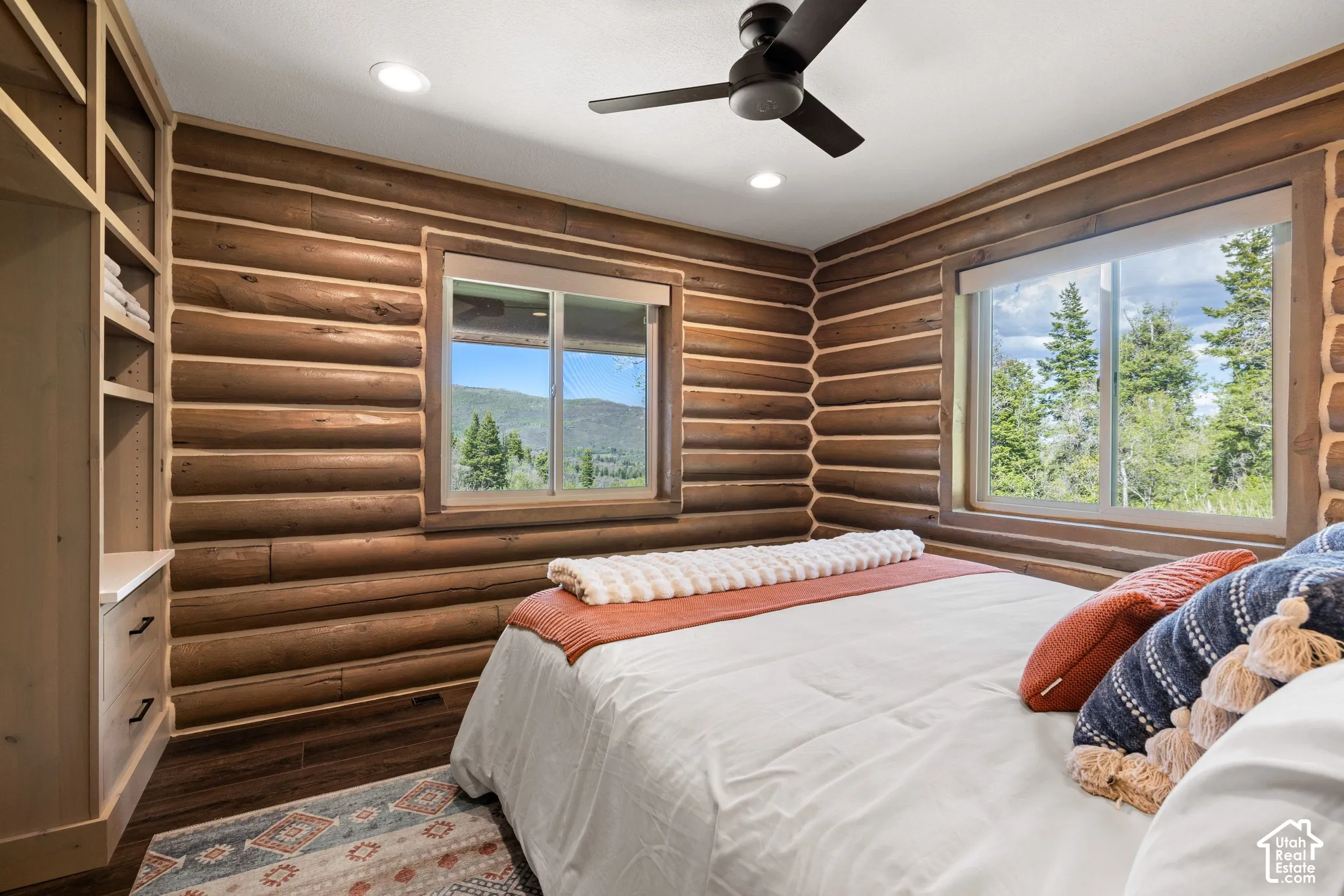 Log walls with integrated windows, wood-finish flooring, built-in shelving, and a ceiling fan