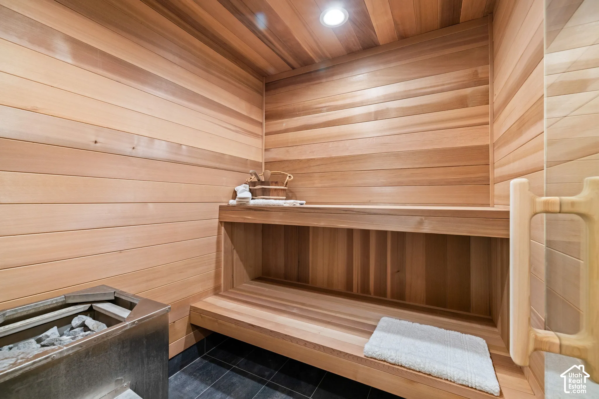 Wood-paneled sauna featuring built-in bench seating, recessed lighting, and a metal sauna heater with stones
