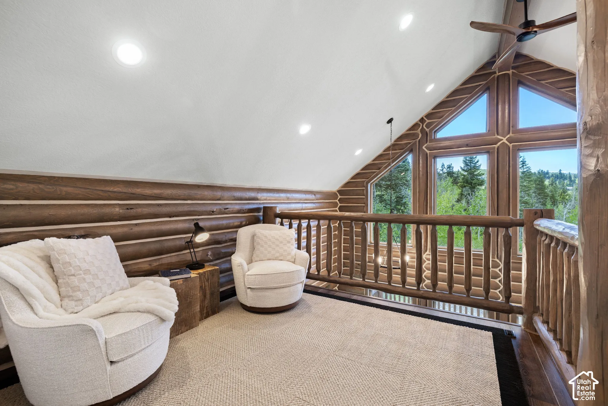 Wood-paneled walls and ceiling, exposed log beams, large windows, recessed lighting, and a ceiling fan