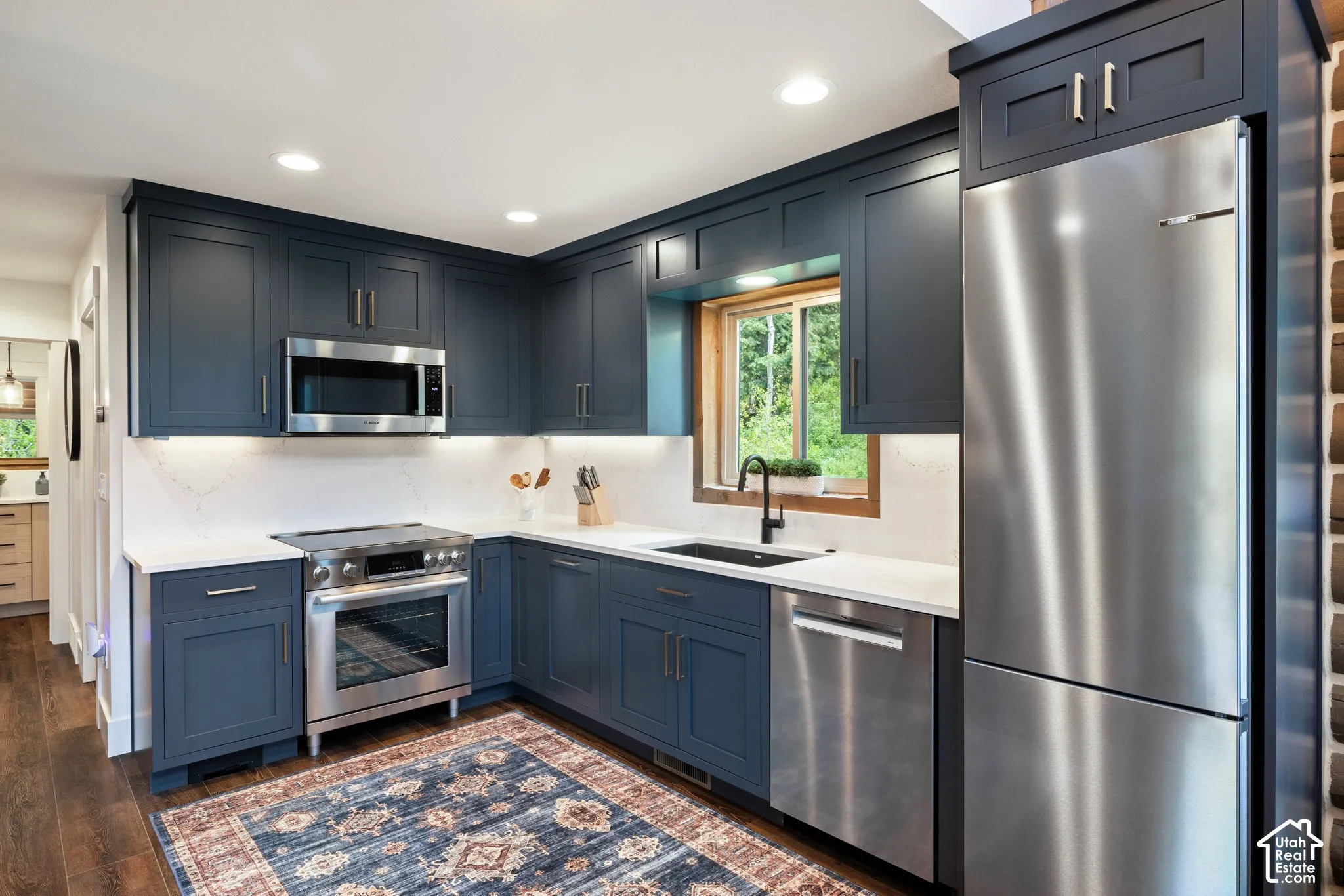 Full-height navy cabinetry, white countertops, stainless steel appliances, wood-finish flooring, and a black sink with a matte black faucet