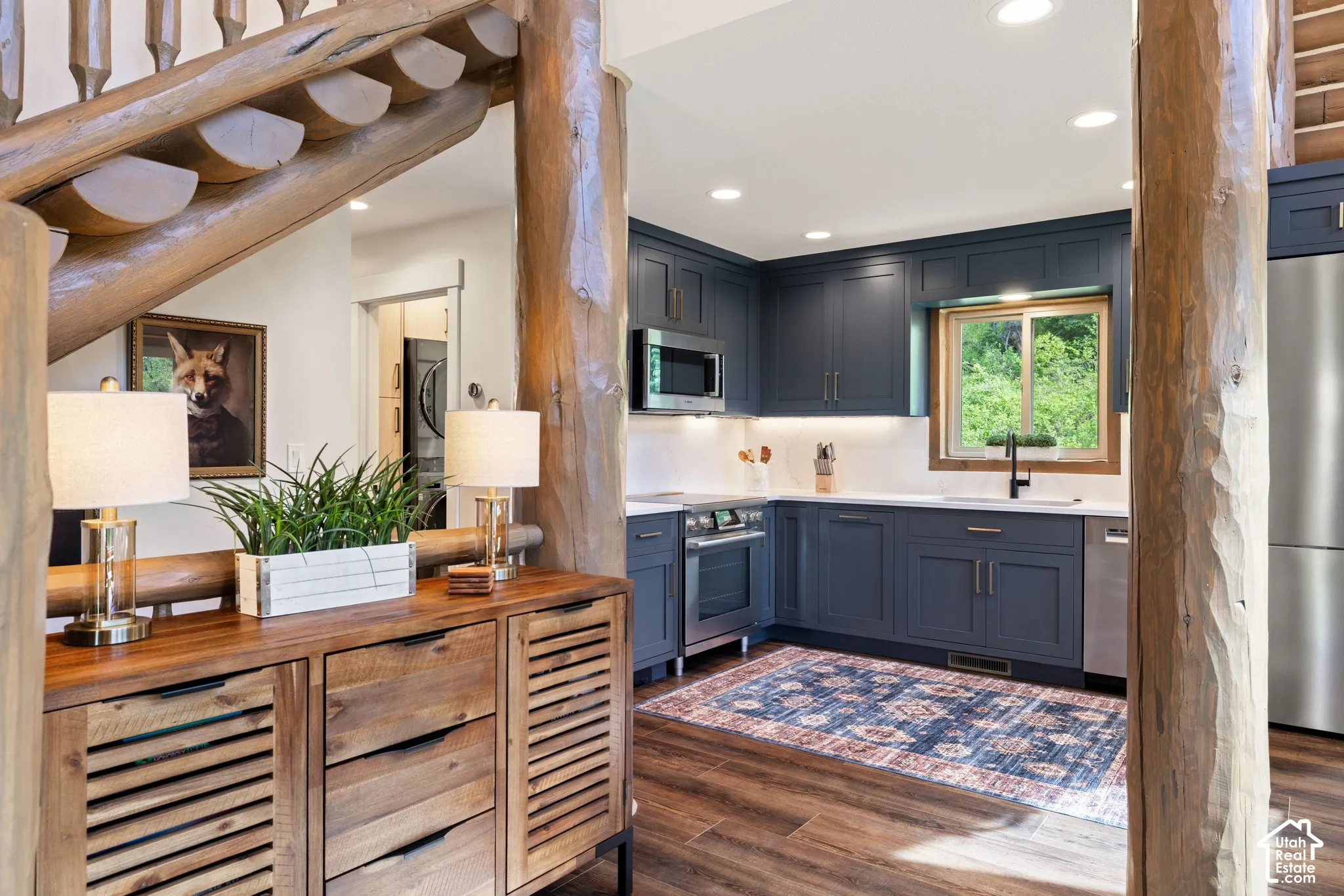 Rustic wood log staircase, wood-finish flooring, kitchen featuring blue cabinetry, stainless steel appliances, and white countertops