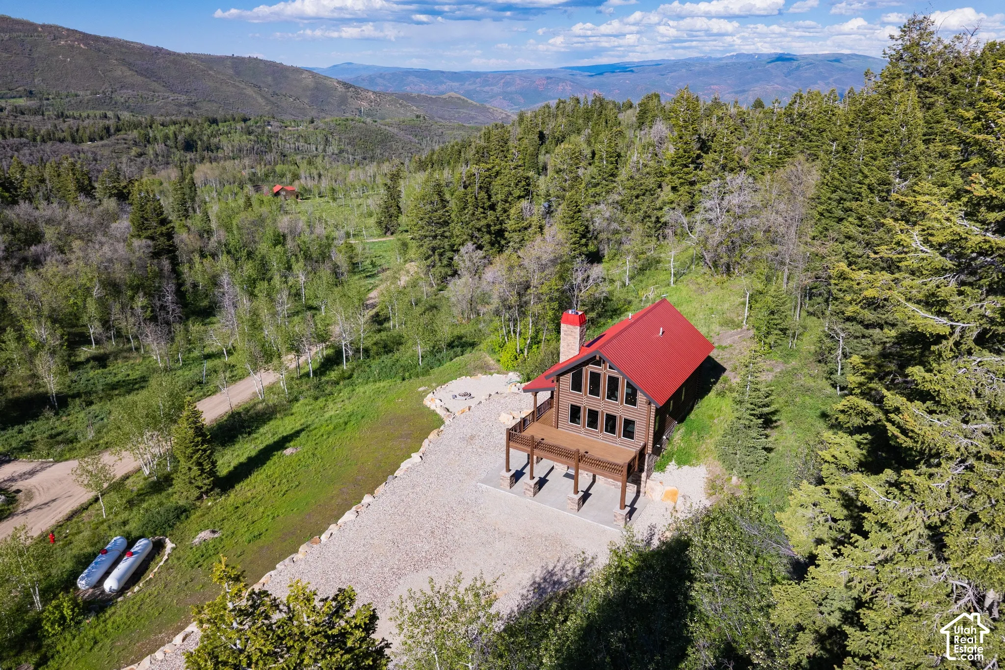 Expansive mountain property featuring a log-sided residence with a red roof, a large exterior deck, and multiple windows