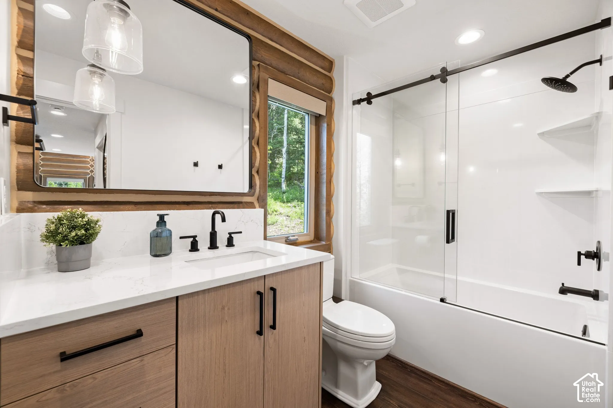 Hardwood-style flooring, a light wood-finish vanity with a white countertop and rectangular undermount sink, and black matte fixtures