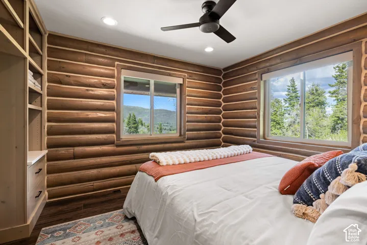 Log walls with integrated windows, wood-finish flooring, built-in shelving, and a ceiling fan