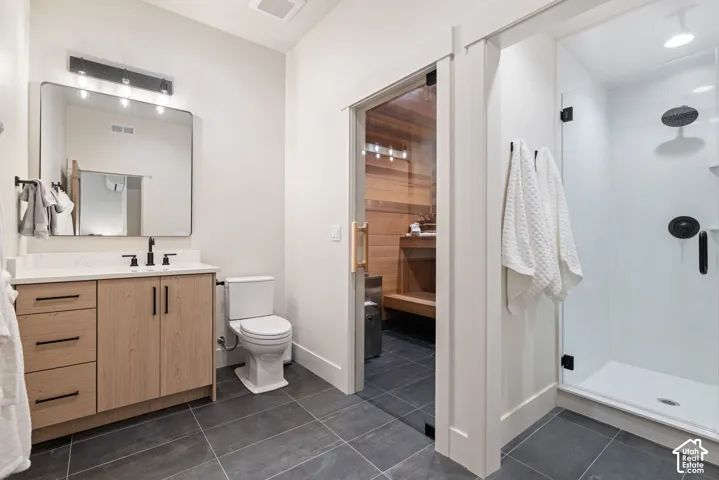 Modern bathroom featuring a wood-finish vanity with a light-toned countertop, a frameless shower with a glass enclosure, and dark tile flooring