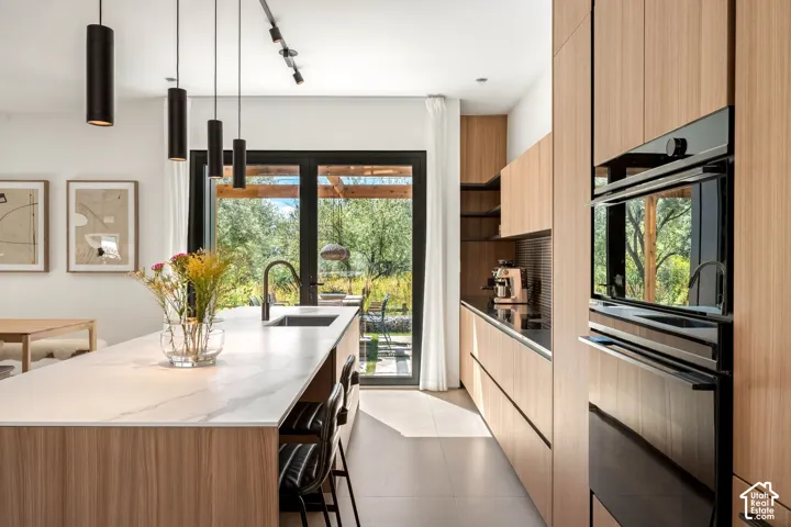 Modern kitchen featuring light wood-finish cabinetry, a large center island with a white countertop, and integrated black appliances