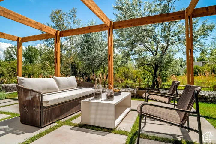 Outdoor living area featuring a wood pergola, concrete paver patio, and lush surrounding greenery