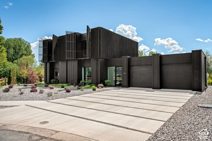 Modern exterior with dark vertical siding, a multi-panel concrete driveway, an integrated two-car garage, and a low-maintenance landscape design with gravel and plantings