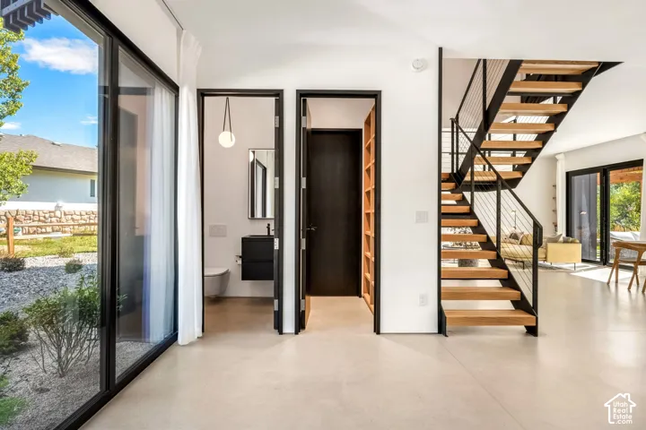 Expansive floor-to-ceiling windows, floating wood staircase with cable railing, light-colored flooring, and a powder room with a wall-mounted vanity