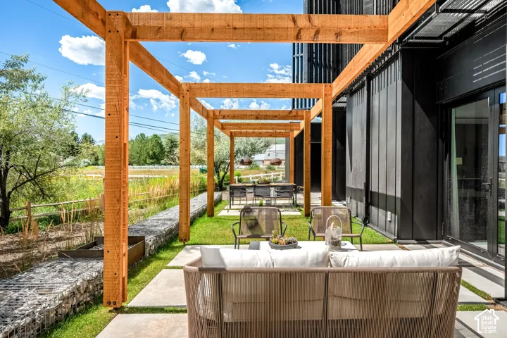 Expansive outdoor patio with wood pergola, dark-toned exterior siding, and concrete paver pathway