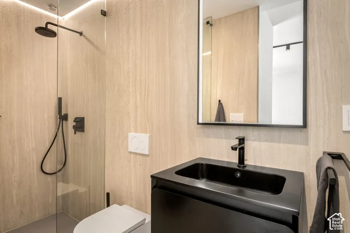 Modern bathroom featuring a glass-enclosed shower with matte black fixtures, an illuminated mirror, and a sleek black vanity with a coordinating sink