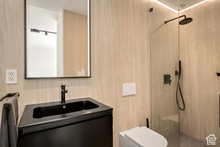 Modern bathroom featuring a black vanity with integrated sink, matte black faucet, illuminated mirror, and a glass-enclosed shower with a rain showerhead