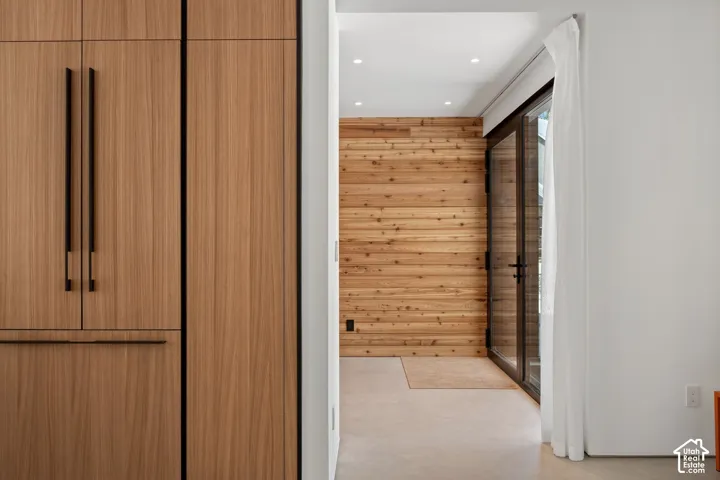 Integrated wood-finish cabinetry, recessed ceiling lighting, wood-paneled accent wall, and glass-panel door