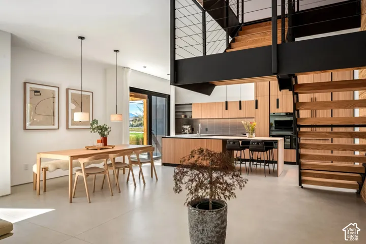 Open-concept living space with light wood-finish flooring, a contemporary kitchen featuring light wood-finish cabinetry, a built-in oven, and a modern industrial-style staircase with wood treads and metal railing