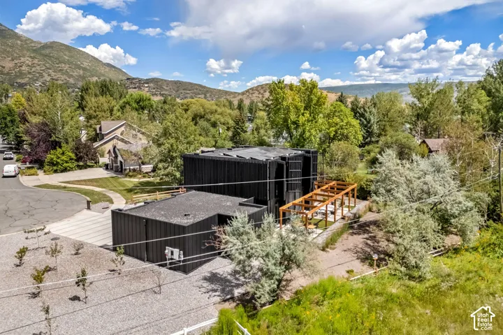 Modern black exterior, multi-level structure, wood pergola, gravel driveway, and surrounding mature trees