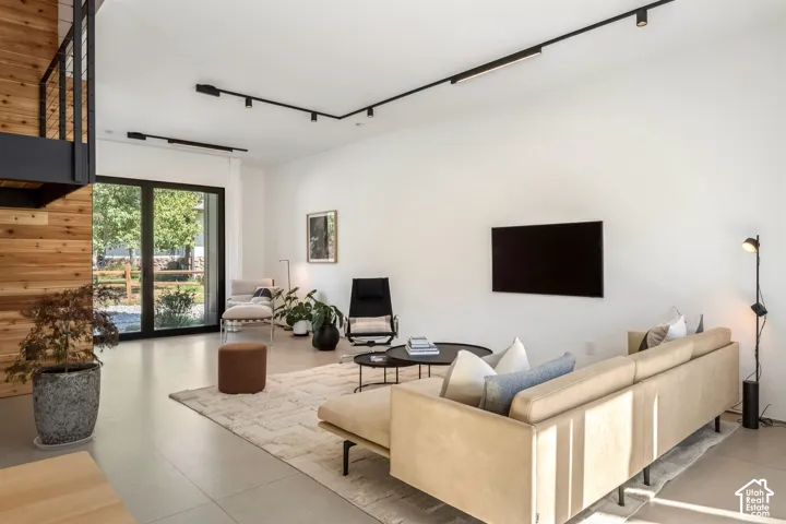 Spacious living area featuring large format tile flooring, black-framed glass sliding doors, wood plank accent wall, and a staircase with metal railing