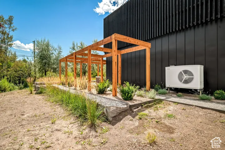 Wood pergola structure with a gravel pathway, complemented by planted garden beds and a modern black exterior wall