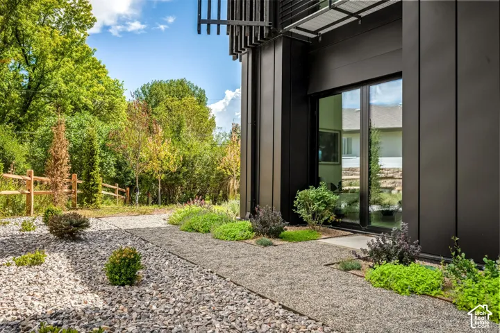 Black vertical panel exterior with large glass sliding doors, front gravel landscaping, and lush perimeter greenery