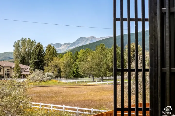 Mountain backdrop, expansive open field, white perimeter fencing, mature trees, adjacent residential architecture