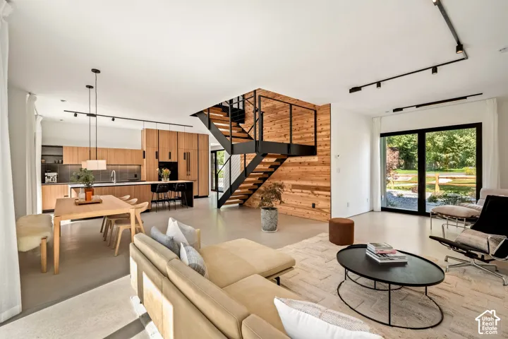 Open-concept living space featuring wood-finish cabinetry, a kitchen island with seating, a modern staircase with black railings, and expansive glass sliding doors