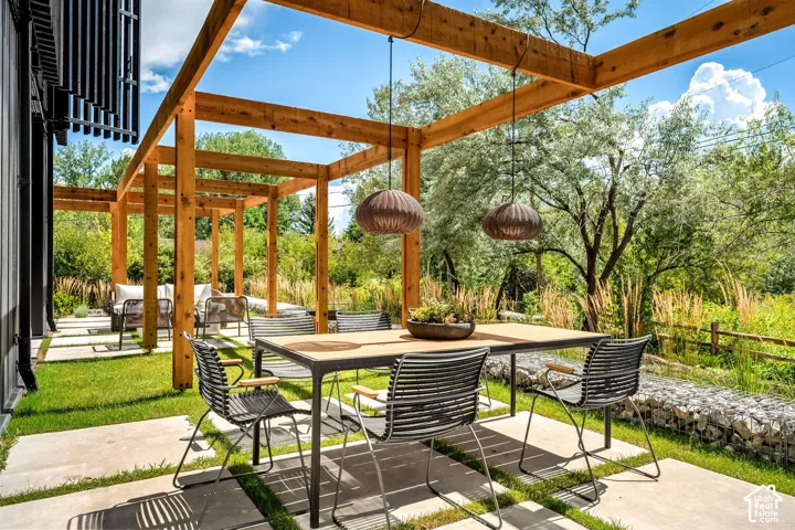 Expansive outdoor space featuring a timber pergola, concrete patio pavers, and a gabion wall