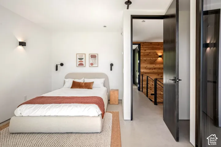 White walls with modern wall sconces, dark wood-finish door, wood-paneled wall, and a staircase with a black metal railing