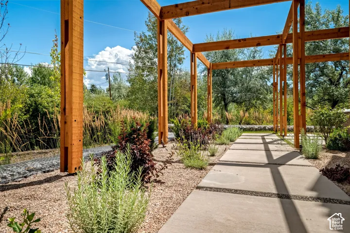Architectural wood pergola, concrete paver pathway, gravel landscaping, mature shrubs, and ornamental grasses
