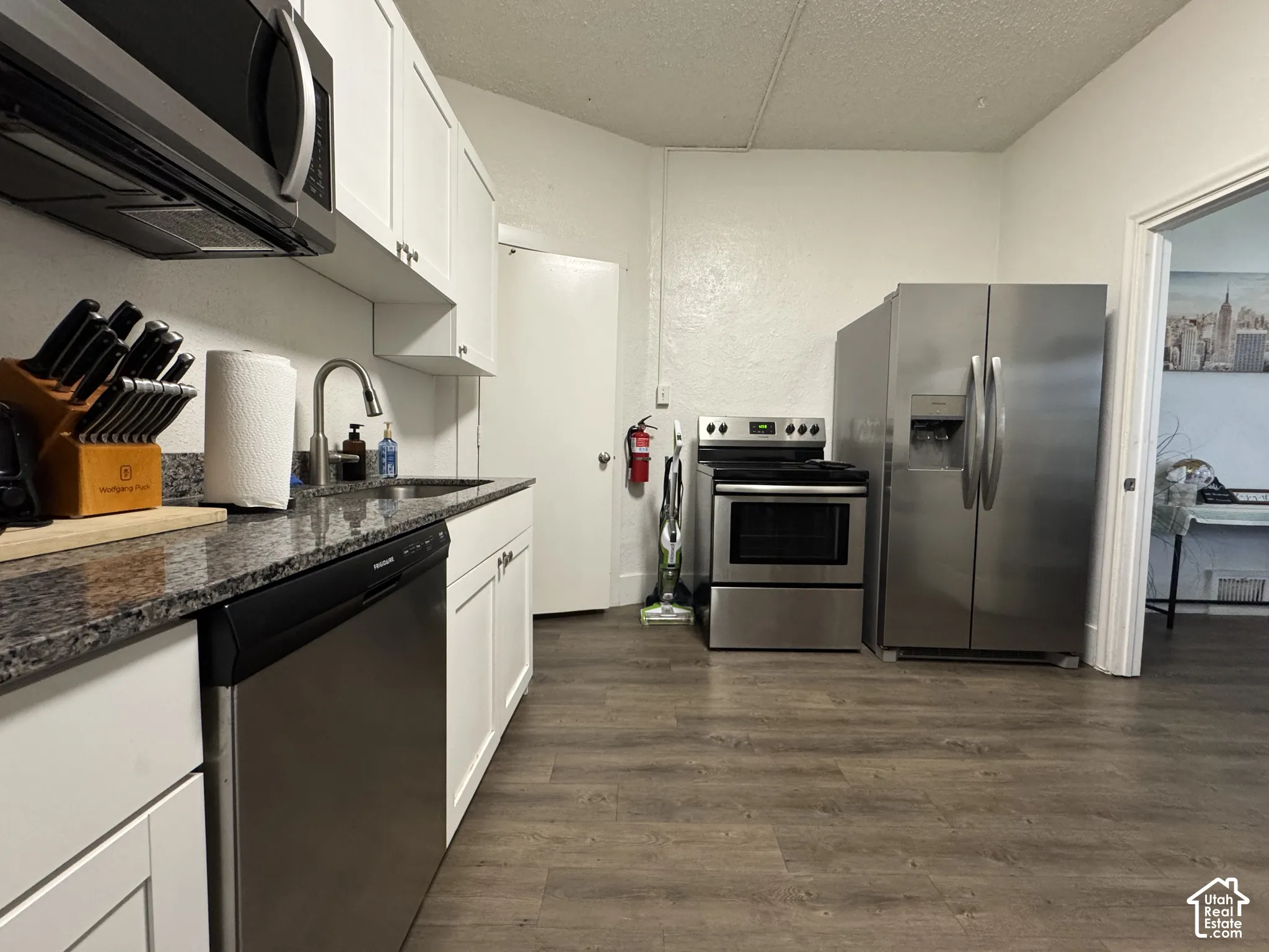 White cabinetry, dark granite-finish countertops, stainless steel appliances, wood-finish flooring, and a stainless steel sink with a gooseneck faucet