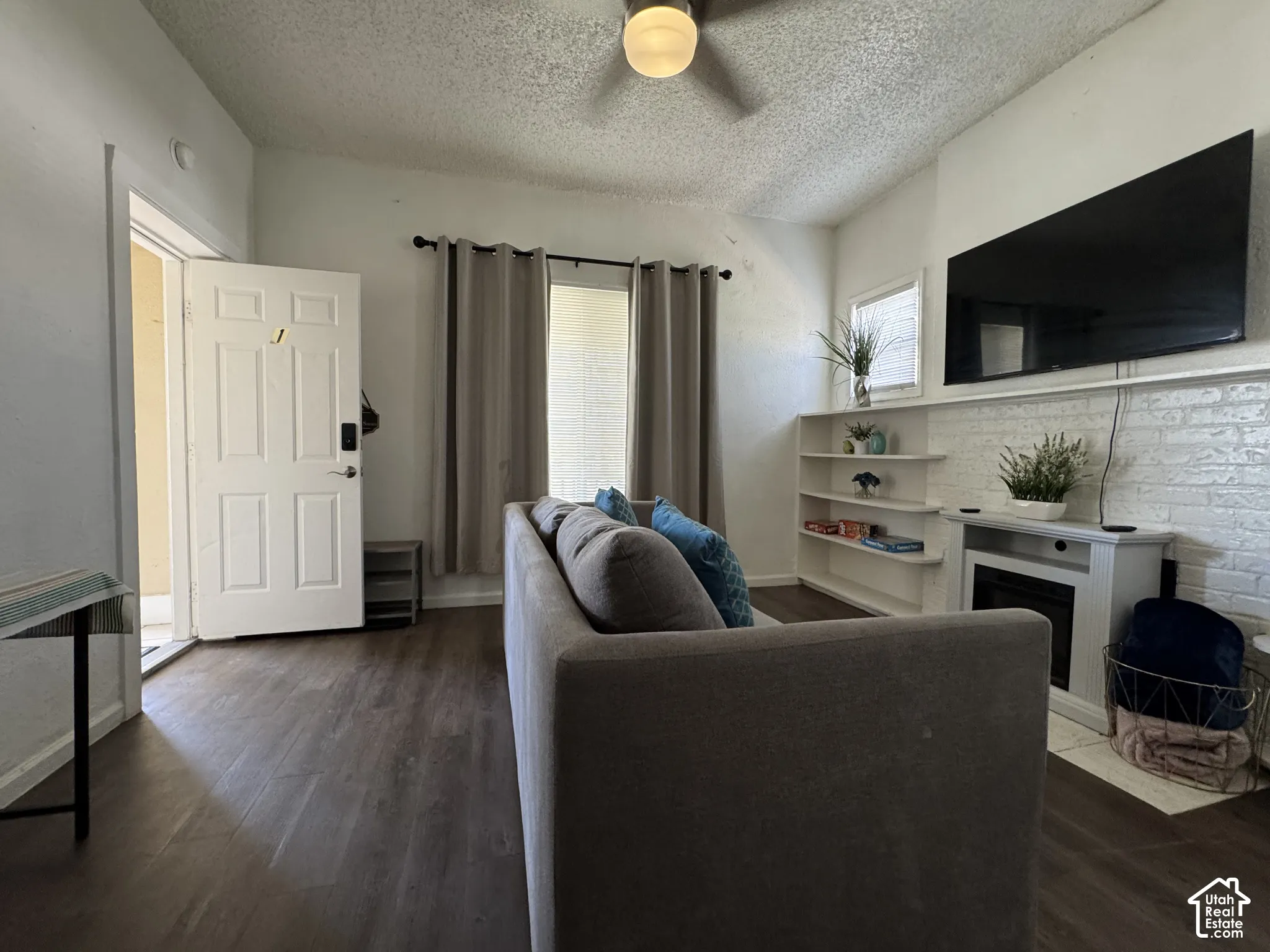 Vaulted ceiling with an attached light fixture, wood-finish flooring, and a white brick-finish accent wall