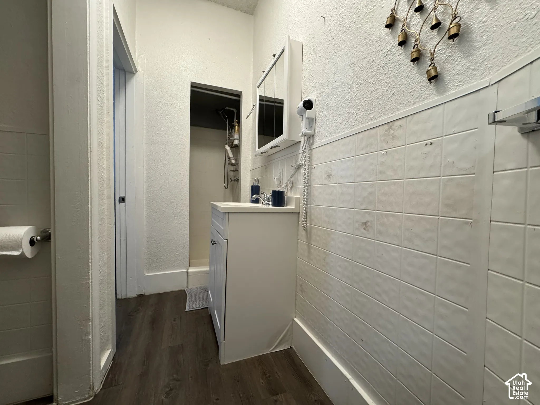 White vanity with a single basin sink, wall-mounted medicine cabinet, wood-finish flooring, and tiled lower walls