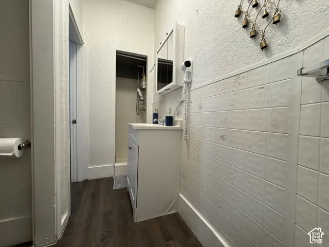 White vanity with a single basin sink, wall-mounted medicine cabinet, wood-finish flooring, and tiled lower walls