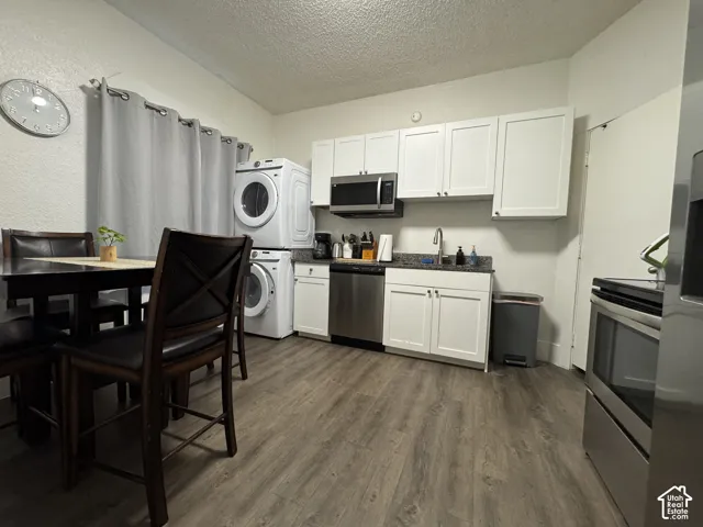 White shaker-style cabinetry, granite-style countertops, stainless steel appliances, wood-finish flooring, and a stacked washer/dryer