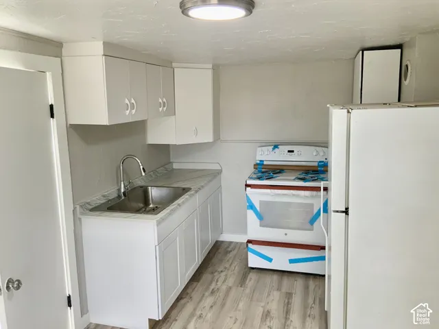 White cabinetry with curved silver-tone hardware, wood-finish flooring, undermount stainless steel sink with a gooseneck faucet, and light-toned countertop