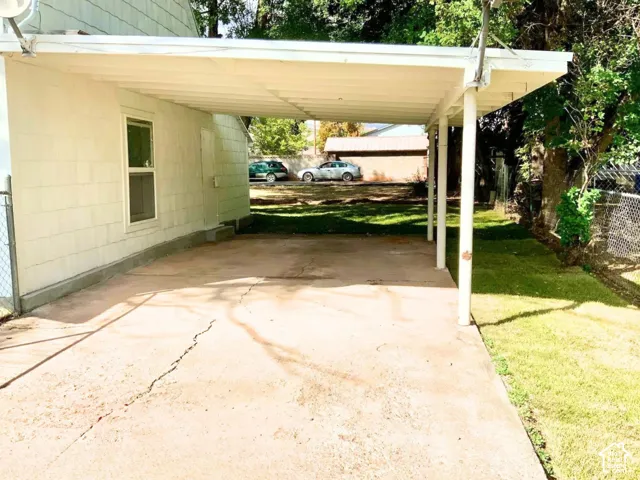 Covered carport structure with support columns, concrete pad, and side yard with established trees