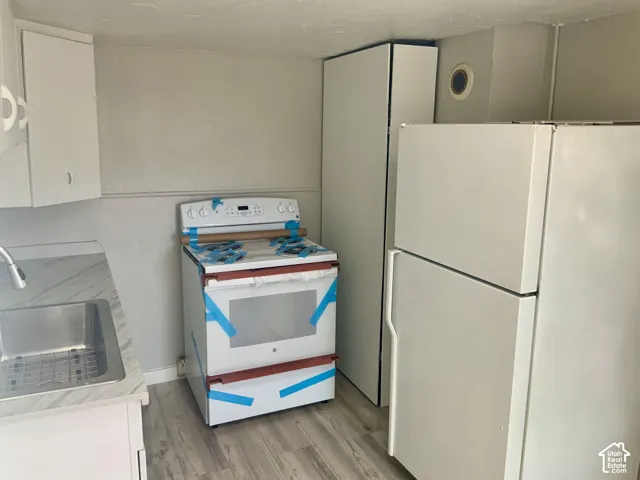 White kitchen cabinetry, stainless steel sink, wood-finish flooring, white freestanding range, and white refrigerator