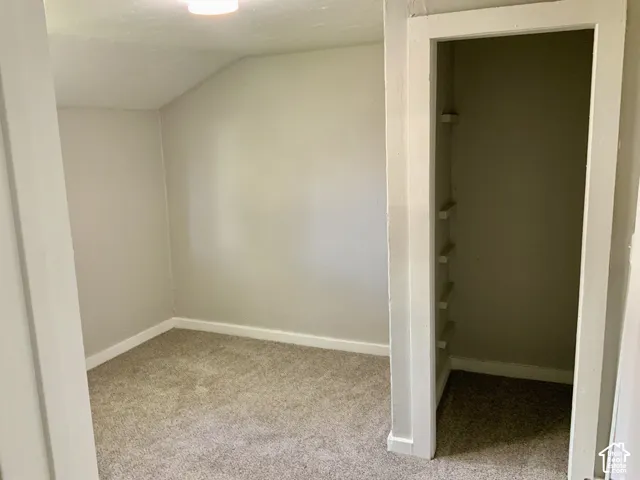 Carpeted room with sloped ceiling, recessed lighting, and an adjacent built-in closet with shelving