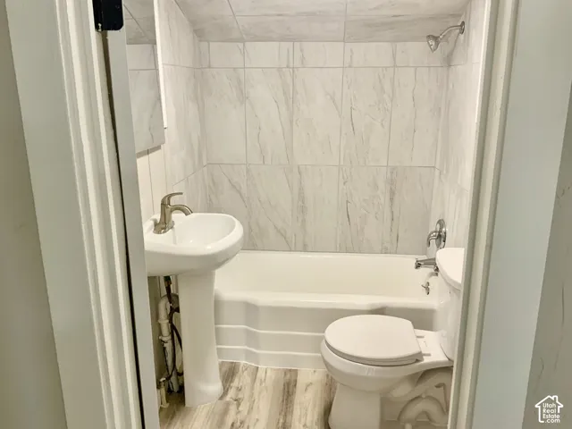 Bathroom with pedestal sink, white bathtub, toilet, and wood-finish flooring