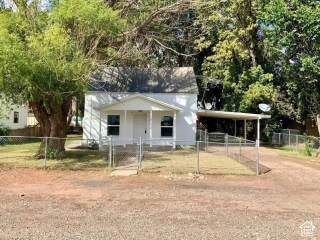 White exterior with a covered front porch, chain-link fence, gravel driveway, and a carport