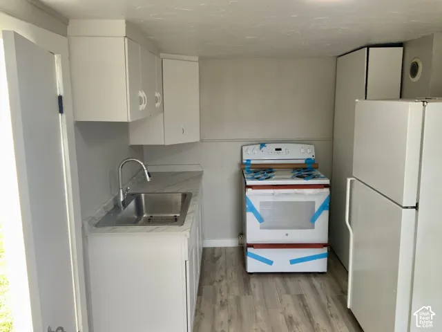Kitchen featuring white cabinetry, stainless steel sink with gooseneck faucet, light grey countertops, and wood-finish flooring