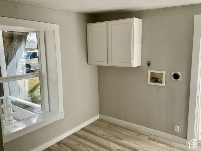 Laminate wood-finish flooring, white wall-mounted cabinetry, window with white trim, light gray painted walls, and laundry hookups