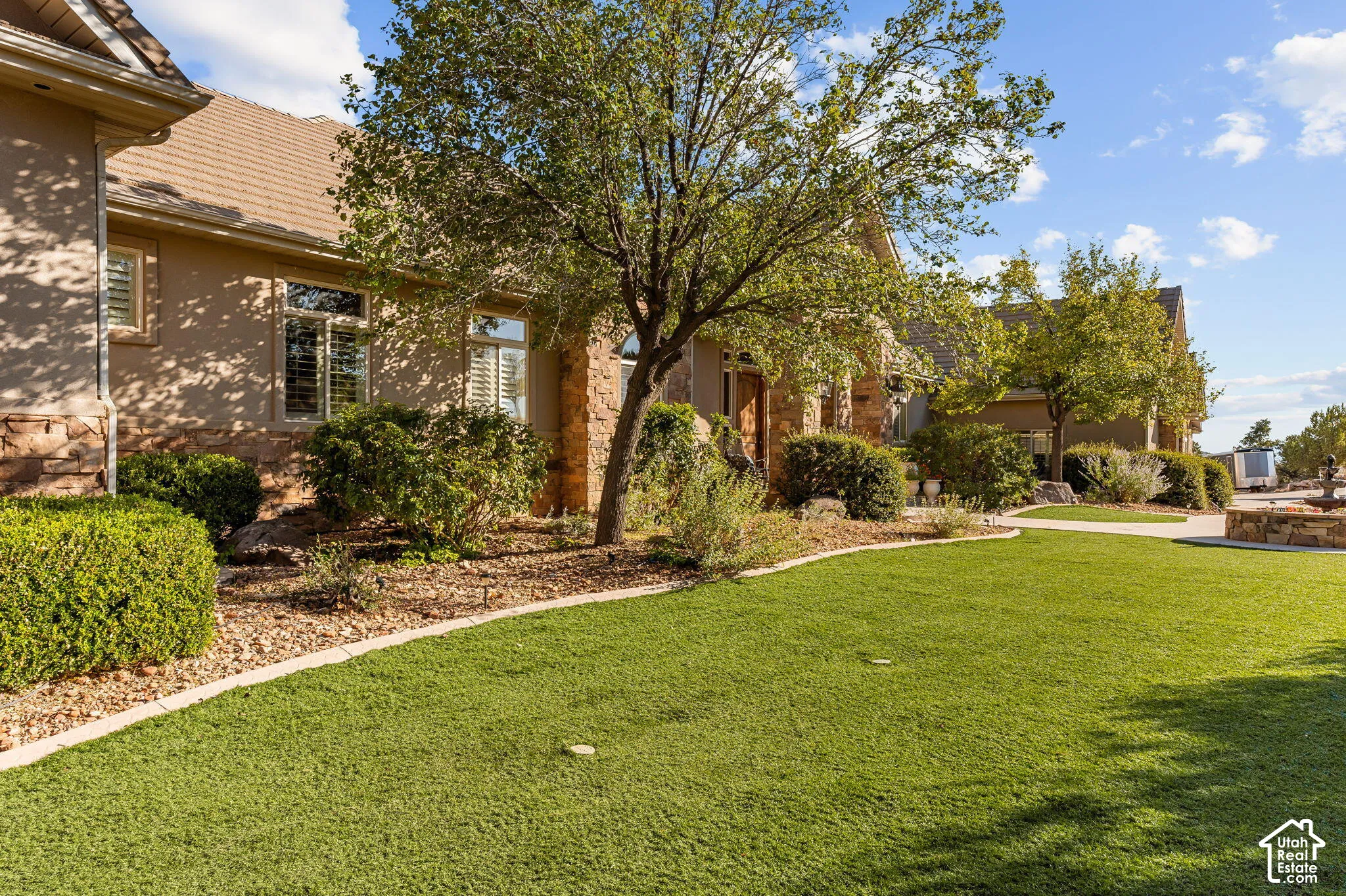 Stucco exterior with stone accents, mature landscaping, manicured lawn, and a stone water feature
